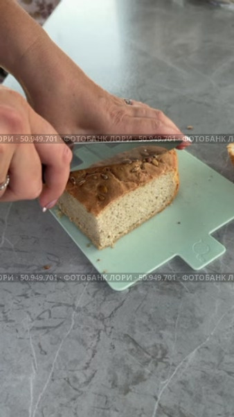 A woman is slicing bread. Close-up of hands holding a knife and the bread. Vertical video. Стоковое видео, видеограф Vadzim Yakubovich / Фотобанк Лори
