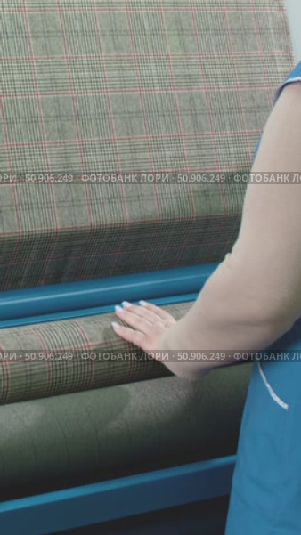 A woman works on a fabric inspection machine in a garment factory, on which a checkered fabric is wound, a person's hand touches the fabric. Стоковое видео, видеограф Дмитрий Нечаев / Фотобанк Лори