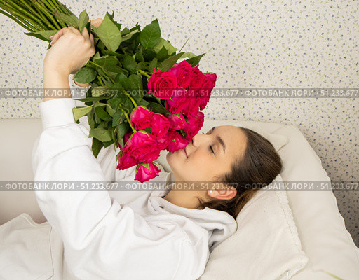 A young and happy girl lies on the bed and smells roses with her eyes closed. Стоковое фото, фотограф Anna Scherbina / Фотобанк Лори