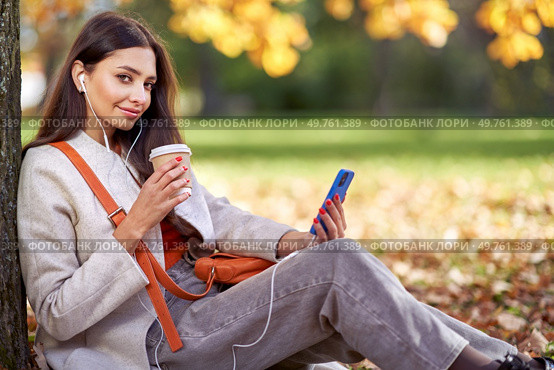 A young beautiful woman walks in the autumn park and talks on the phone. A girl with a smartphone takes photos in an autumn forest. Стоковое фото, агентство Ingram Publishing / Фотобанк Лори