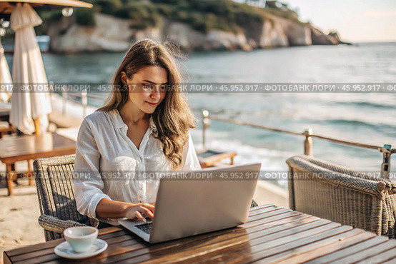 A young female freelance businessman is working on a laptop while on vacation by the sea or shopping in an online store. Стоковое AI-изображение, AI-художник Photojuli / Фотобанк Лори