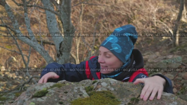 A young female hiker attempts to climb a moss-covered rock surrounded by a serene natural landscape of trees and undergrowth. Gives up and cannot climb. Стоковое видео, видеограф Воловодов Владимир / Фотобанк Лори