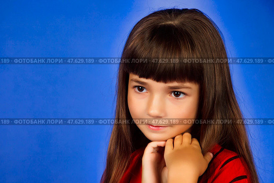 A young girl with striking long hair and bangs poses thoughtfully against a bright blue background. She embodies innocence and charm, capturing the essence of childhood wonder in her expression. Стоковое фото, фотограф Aleksandr Golubev / Фотобанк Лори