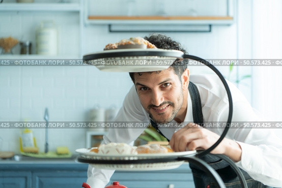 A young man puts on an apron to make dessert to eat with his wife. Checking the completeness of the finished dessert. Стоковое фото, агентство Ingram Publishing / Фотобанк Лори