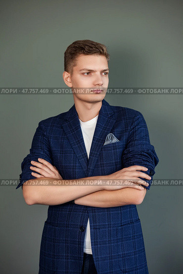 A young man stands confidently with his arms crossed, wearing a tailored blazer and a casual shirt. The modern backdrop captures the essence of Dubai's vibrant style and culture. Стоковое фото, фотограф Aleksandr Golubev / Фотобанк Лори