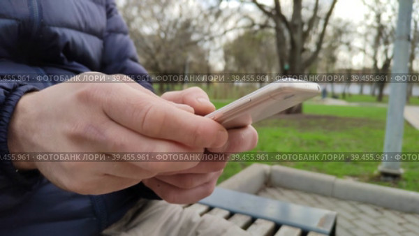 A young man types a text message, or makes online purchases, or downloads a smartphone app. A mobile phone in men's hands. Social networks and marketplaces in the modern world. Стоковое видео, видеограф Ирина / Фотобанк Лори