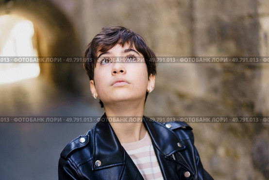 A young woman in a stylish leather jacket stands confidently in an urban setting, gazing thoughtfully upward, capturing a serene moment of introspection amidst the citys vibrant hustle. A Contemplative Young Woman Dressed in a Stylish Leather Jacket Deeply Looking Upwards. Стоковое фото, агентство Ingram Publishing / Фотобанк Лори