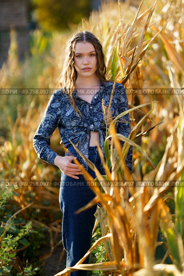 A young woman stands confidently in a vast cornfield, donning a chic and stylish outfit, perfectly complemented by the tall, golden stalks that surround her during a breathtaking sunset. A beautiful portrait of a young woman in a cornfield during a stunning sunset scene. Стоковое фото, агентство Ingram Publishing / Фотобанк Лори