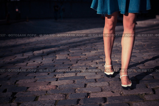 A young woman wearing a skirt and retro shoes is walking on a cobbled street at sunset. Стоковое фото, агентство Ingram Publishing / Фотобанк Лори