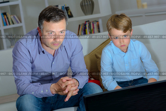 Adult and child engrossed watching television. Стоковое фото, агентство Ingram Publishing / Фотобанк Лори