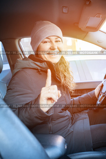 Adult female driver gesturing with forefinger before driving a car, woman wearing winter clothes. Стоковое фото, фотограф Кекяляйнен Андрей / Фотобанк Лори