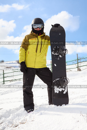 Adult snowboarder in a winter helmet and protective glasses dressed in a snowboarding coat posing with a snowboard outdoor, looking at a camera. Стоковое фото, фотограф Кекяляйнен Андрей / Фотобанк Лори