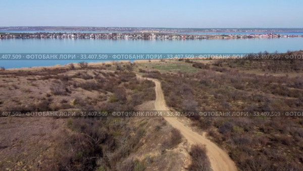 Aerial view, flying over a dirt road in steppe, in the background the pond and village. Camera moving forwards above steppe to the pond side. Khadzhibey Estuary, Odessa region, Ukraine. Стоковое видео, видеограф Некрасов Андрей / Фотобанк Лори
