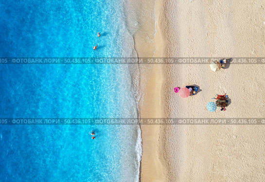Aerial view of adriatic sea, waves, sandy beach and umbrellas with lying people at sunset in summer. Tropical landscape with clear turquoise water. Top view from drone. Lefkada island, Greece. Travel. Стоковое фото, агентство Ingram Publishing / Фотобанк Лори