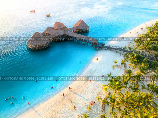 Aerial view of beautiful bungalow in Indian ocean at sunset in summer. Restaurant on the sea. Top view of wooden hotel, palm trees, azure water, white sandy beach. Luxury resort in Kendwa, Zanzibar. Стоковое фото, агентство Ingram Publishing / Фотобанк Лори