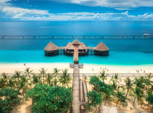 Aerial view of bungalow, white sandy beach, ocean on summer sunny day. Restaurant on the sea. Top drone view of wooden hotel, azure water, palms, sky with clouds. Luxury resort in Kendwa, Zanzibar. Стоковое фото, агентство Ingram Publishing / Фотобанк Лори