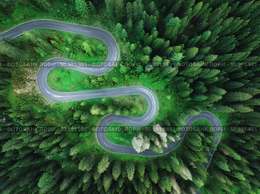 Aerial view of mountain curvy road and green forest in summer. Dolomites, Italy. Top view of winding road on mountain pass, trees in spring.  Snake road through the woods. Moody landscape with roadway. Стоковое фото, агентство Ingram Publishing / Фотобанк Лори