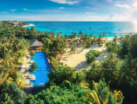 Aerial view of palms, pool, bungalow, sandy beach, umbrellas, yachts, boats, blue ocean, sky with clouds at sunset. Summer vacation in Kendwa, Zanzibar island. Tropical landscape. Clear sea. Top view. Стоковое фото, агентство Ingram Publishing / Фотобанк Лори