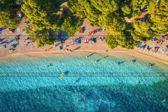 Aerial view of sandy beach with colorful umbrellas, swimming people, clear sea bay with transparent blue water and green trees at sunset in summer. Travel in Croatia, Adriatic sea. Top view. Seascape. Стоковое фото, агентство Ingram Publishing / Фотобанк Лори