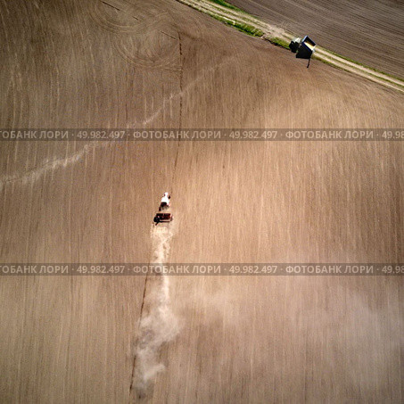 Aerial view of the tractor plowing spring field, a column of dust stretches behind the tractor, Ukraine. Photo from the drone. Aerial view tractor with a cultivator for seeds at the beginning of the spring season of agricultural work. Стоковое фото, агентство Ingram Publishing / Фотобанк Лори