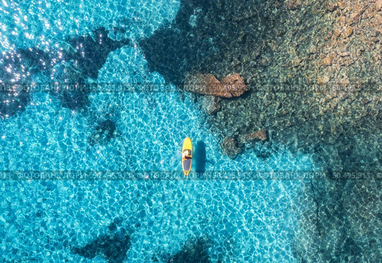 Aerial view of with man on sup board in blue sea at sunset in summer. Man on floating canoe in transparent azure water. Kayak. Sardinia island, Italy. Tropical seascape. Active travel. Drone view. Стоковое фото, агентство Ingram Publishing / Фотобанк Лори