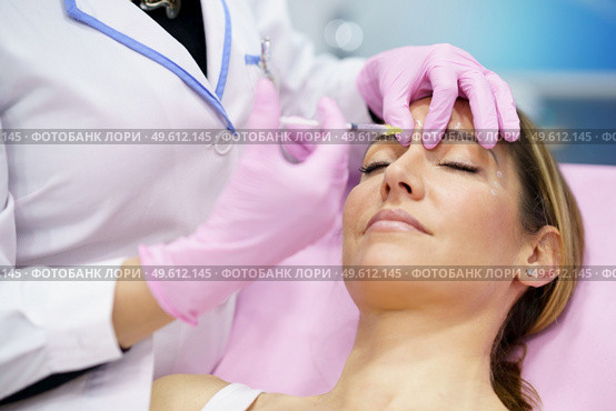 Aesthetic doctor injecting botulinum toxin into the forehead of her middle-aged patient. Facial treatment done in a cosmetic surgery clinic.. Aesthetic doctor injecting botulinum toxin into the forehead of her middle-aged patient. Стоковое фото, агентство Ingram Publishing / Фотобанк Лори