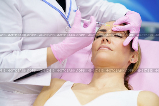Aesthetic doctor injecting botulinum toxin into the forehead of her middle-aged patient. Facial treatment done in a cosmetic surgery clinic.. Aesthetic doctor injecting botulinum toxin into the forehead of her middle-aged patient. Стоковое фото, агентство Ingram Publishing / Фотобанк Лори
