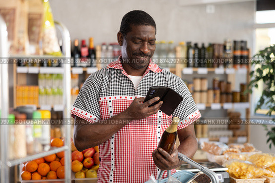 African man customer at shop scans QR code on beer bottle using phone camera. Стоковое фото, фотограф Яков Филимонов / Фотобанк Лори