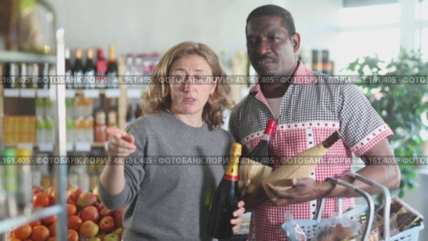 African man with European wife hold bottle and choose alcohol wine bottle in storeEuropean woman with African husband took different varieties of alcohol from shelf, choose wine light alcohol beverage. Client hesitates before buying, chooses alcohol, reads labels on bottles. Стоковое видео, видеограф Яков Филимонов / Фотобанк Лори