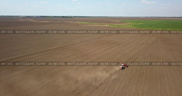 Agricultural works at farmlands. A tractor with a cultivator sowed a field. A farmer’s activity at the beginning of the spring season. Photo from the drone. Tractor cultivates the field, spring works on farmlands. Photo from the drone. Стоковое фото, агентство Ingram Publishing / Фотобанк Лори
