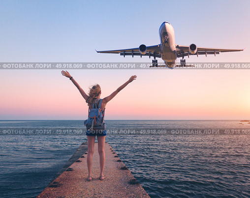 Airplane and woman at sunset. Summer landscape with girl standing on the sea pier with raised up arms and flying passenger airplane. Woman and landing commercial plane in the dusk.Lifestyle and travel. Стоковое фото, агентство Ingram Publishing / Фотобанк Лори