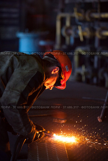 Aksu, Pavlodar region, Kazakhstan - May 29, 2012: Aksu steam power station. Welder worker in orange hardhat welding metal grid floor. Редакционное фото, фотограф Alexey Rezvykh / Фотобанк Лори