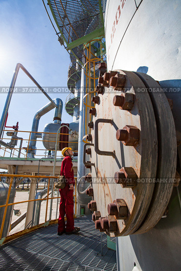 Aktobe region/Kazakhstan - May 04 2012: Oil refinery plant. Technician in red work wear and yellow helmet on refining column. CNPC company. Редакционное фото, фотограф Alexey Rezvykh / Фотобанк Лори
