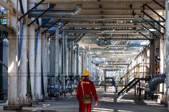 Aktobe region/Kazakhstan - May 04 2012: Refinery worker in red work wear and yellow helmet under the pipelines. Oil refinery plant. CNPC-AMG company. Редакционное фото, фотограф Alexey Rezvykh / Фотобанк Лори