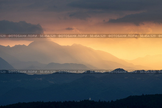Amazing silhouettes of a mountains at colorful sunset in summer in Slovenia. Landscape with mountain ridges in fog, golden sunlight and clouds in the evening. Nature. Hills in sunlight. Scenery. Стоковое фото, агентство Ingram Publishing / Фотобанк Лори