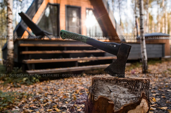An axe will be stuck into a wooden log. Harvesting firewood for the winter season. Logging on the background of a country house. Lumber, wood-cutting tools. Стоковое фото, фотограф Photojuli / Фотобанк Лори