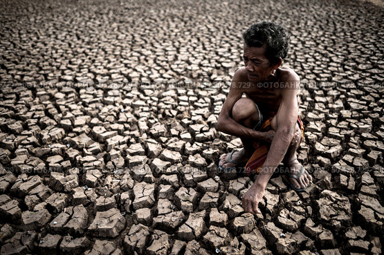 An elderly man sitting hugging his knees bent at the barren ground,global warming. Стоковое фото, агентство Ingram Publishing / Фотобанк Лори