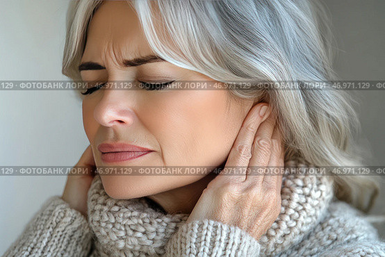 An elderly woman with gray hair holds her ears, experiencing obvious discomfort or pain. Her face expresses tension, and her eyes are closed. She is wearing a warm knitted sweater and a scarf, which may indicate a cold season or a cold. The background is neutral, which emphasizes the woman's emotions and condition. The image conveys a feeling of pain, malaise, or hearing problems. Стоковое AI-изображение, AI-художник Анна Кривицкая / Фотобанк Лори