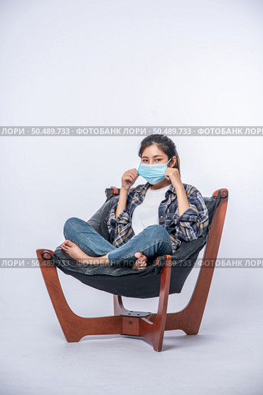 An uncomfortable woman sitting on a chair and wearing a mask. Стоковое фото, агентство Ingram Publishing / Фотобанк Лори