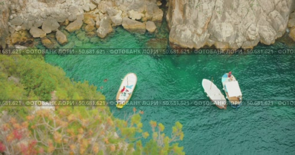 Anchored boats and swimmers in scenic emerald water cove in summer Capri Island. Стоковое видео, видеограф Igor Tichonow / Фотобанк Лори