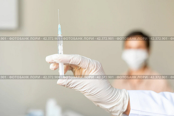 Anonymous healthcare worker vaccinating middle-aged female patient. Blurred background. Стоковое фото, фотограф Natalia Gdovskaia / Фотобанк Лори