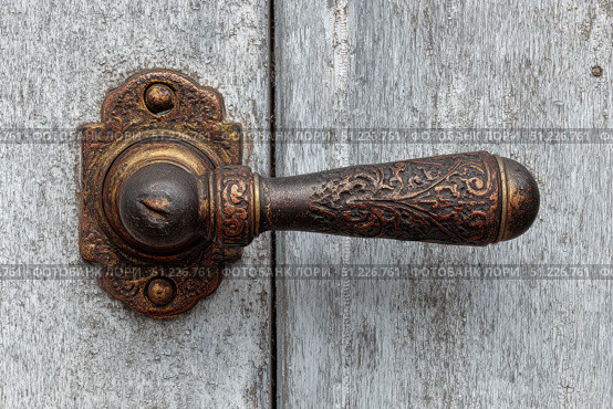 Antique Door Knob. Ornate wooden door with intricate carving metal handle. Faded gray wood. Elaborately fancy cabinet. Old furniture. Traditional architecture design. Decorative wrought iron metalwork. Стоковое AI-изображение, AI-художник Марина Демидюк / Фотобанк Лори