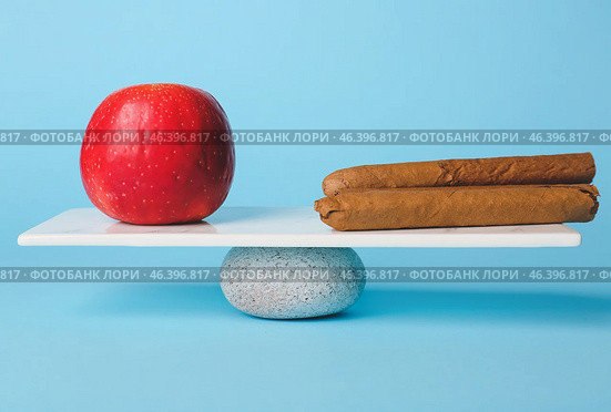 Apple and cigars on teeterboard against color background. Concept of balance. Стоковое фото, фотограф Pixel_shot / Фотобанк Лори