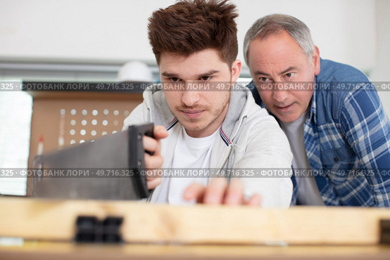 apprentice carpenter using a saw under supervision. Стоковое фото, агентство Ingram Publishing / Фотобанк Лори