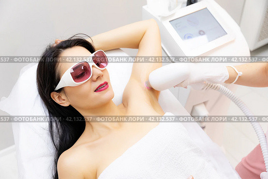 Armpits laser treatment. Close up shot of a young woman having armpits hair removed with a laser hair removal machine by a professional beauty therapist at the beauty spa salon depilation epilation. Стоковое фото, фотограф Ирина Михайличенко / Фотобанк Лори