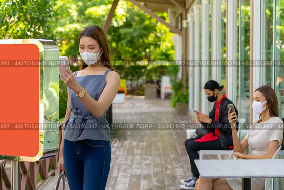 Asian woman using mobile phone scanning for self service online queue on kiosk in front of restaurant. Online technology new normal restaurant concept. Стоковое фото, агентство Ingram Publishing / Фотобанк Лори