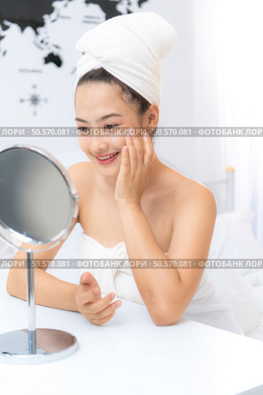 Asian young woman with towel wrapped on head and body applying makeup after shower, Morning beauty routine before work. Стоковое фото, агентство Ingram Publishing / Фотобанк Лори