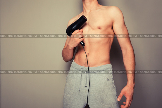 Athletic young man is holding a hair dryer and messing around with it. Стоковое фото, агентство Ingram Publishing / Фотобанк Лори
