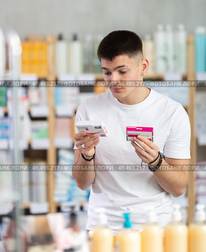 Attentive interested young guy client choosing between two boxes of paracetamol antipyretic pills in drug store. Стоковое фото, фотограф Яков Филимонов / Фотобанк Лори