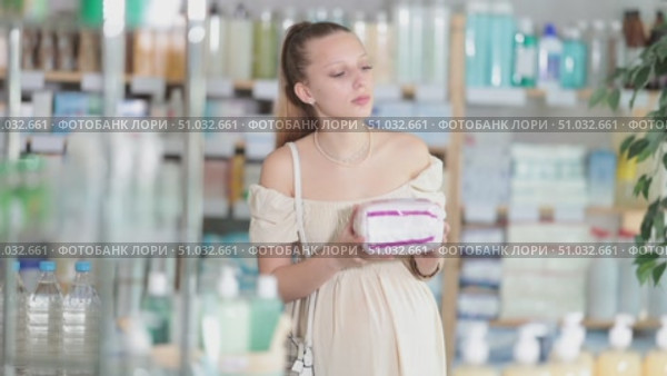 Attentive pregnant woman holding feminine pads trying to make choice in drugstore. Стоковое видео, видеограф Яков Филимонов / Фотобанк Лори